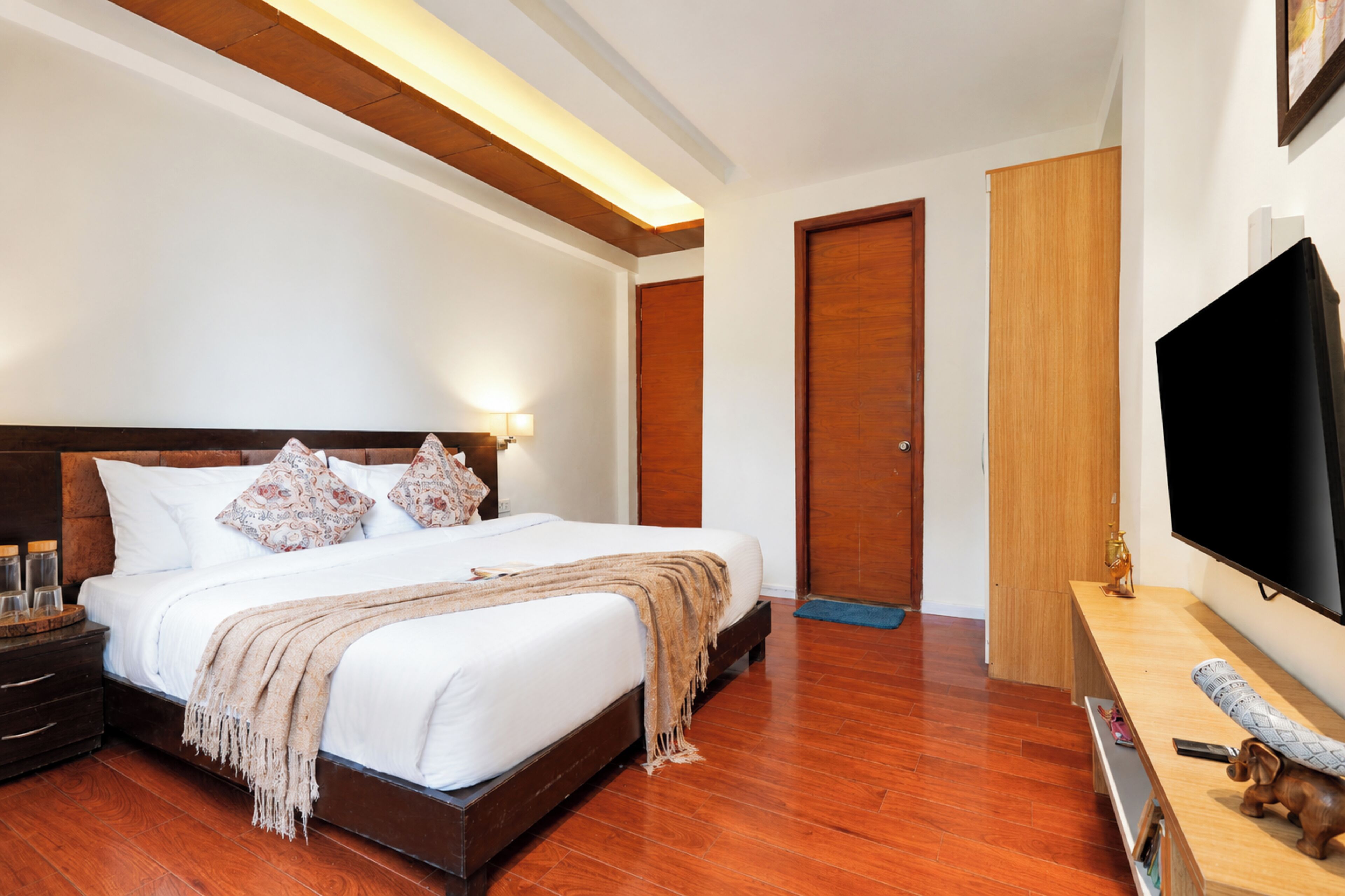 A hotel room with a large bed, wooden flooring, a flat-screen TV, and a wooden wardrobe.
