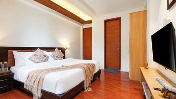 A hotel room with a large bed, wooden flooring, a flat-screen TV, and a wooden wardrobe.