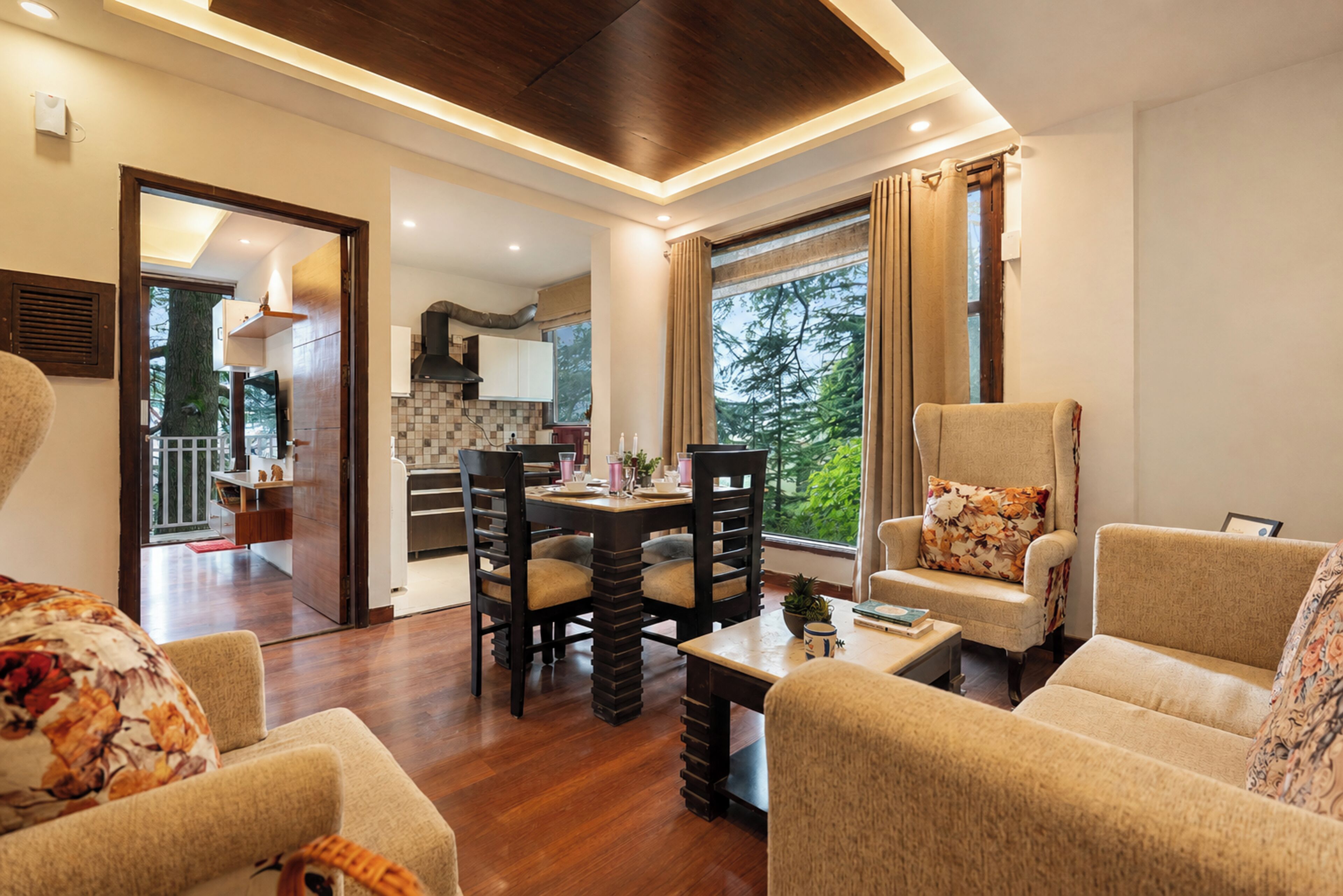 A spacious living area with a wooden floor, a dining table with chairs, and a view of the outdoors through large windows.
