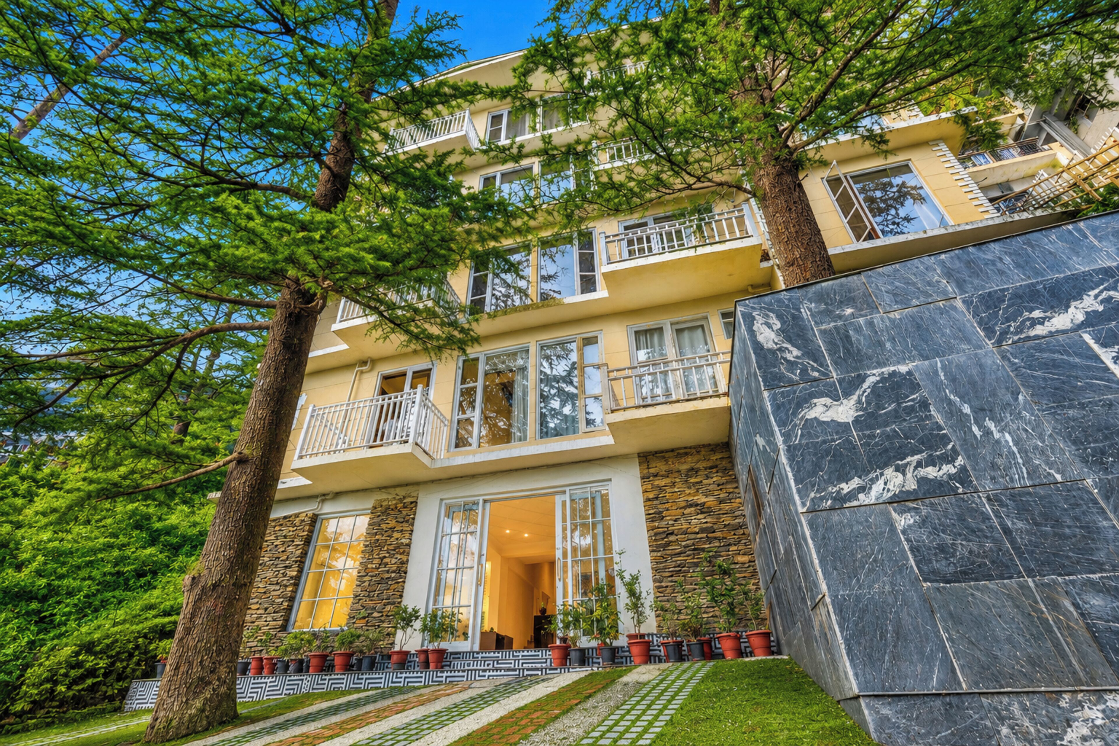 A multi-story building with balconies, a stone facade, and a well-maintained lawn.