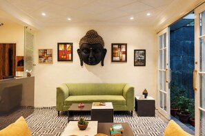 Ein Empfangsbereich mit einem grünen Sofa, einem Buddha-Kopf-Skulptur und gerahmten Kunstwerken an der Wand.