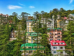 A multi-story residential building with balconies, surrounded by dense green trees.