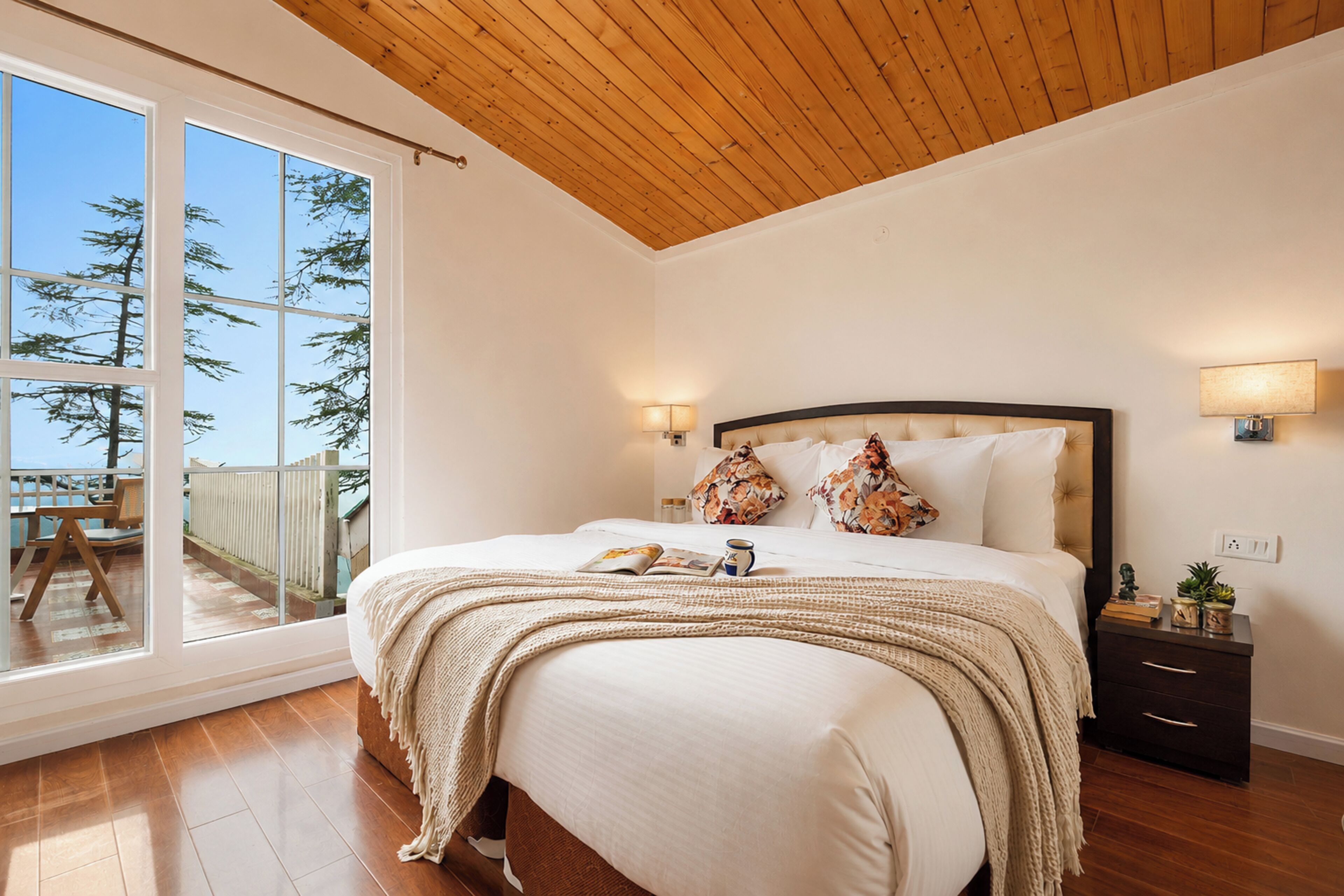 Un dormitorio con una cama grande, una mesita de noche, una lámpara y vistas al exterior a través de una puerta corrediza.