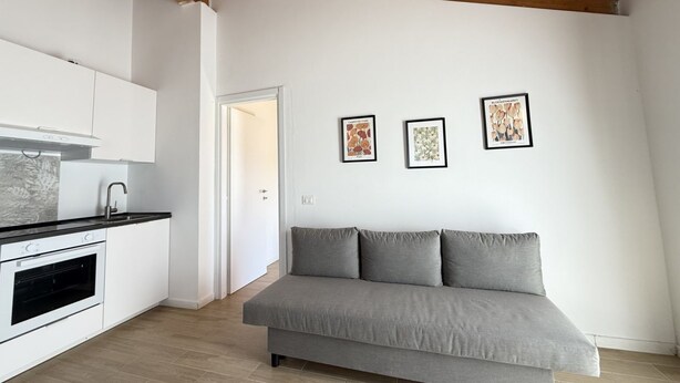 Eine moderne Küche mit weißen Schränken und einem grauen Sofa in einem Wohnbereich.