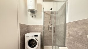 Ein modernes Badezimmer mit einer Duschkabine aus Glas, einer integrierten Waschmaschine und einem wandmontierten Waschbecken.