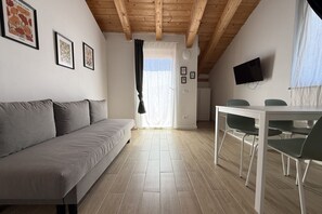 Ein modernes Interieur mit einer Couch, einem Esstisch mit Stühlen, einem an der Wand befestigten Fernseher und gerahmten Bildern.