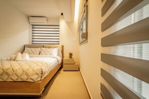 Une chambre à coucher comprenant un lit, des tables de chevet, un climatiseur et une fenêtre avec des stores.