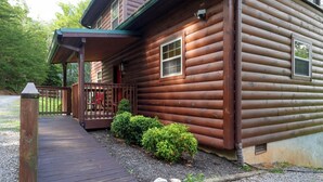 A wooden cabin with a porch, a gravel pathway, and a small garden area. - Gorgeous log cabin that sleeps 7 with hot tub, firepit, exclusive hiking trails! (Sevierville)
