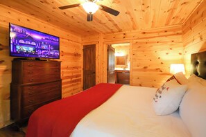 A wooden cabin room with a bed, a dresser, a television, and a ceiling fan. - Gorgeous log cabin that sleeps 7 with hot tub, firepit, exclusive hiking trails! (Sevierville)