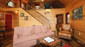 A wooden interior with a staircase, a leather armchair, a patterned sofa, and a table with a document. - Gorgeous log cabin that sleeps 7 with hot tub, firepit, exclusive hiking trails! (Sevierville)
