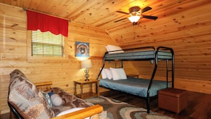 A cozy cabin room with a bunk bed, a small table with a lamp, a red curtain, and a wall-mounted ceiling fan. - Gorgeous log cabin that sleeps 7 with hot tub, firepit, exclusive hiking trails! (Sevierville)