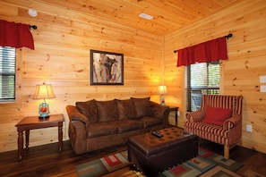 Interior acogedor de una cabaña con un sofá de cuero marrón, un sillón a rayas y un cuadro en la pared.