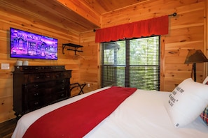 Ein Zimmer in einer Holzhütte mit einem Bett, einem Fernseher und einem Fenster mit Jalousien.