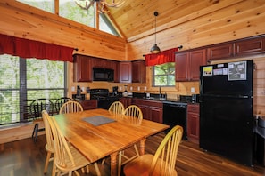 Cocina de cabaña de madera con una mesa de comedor, sillas, un refrigerador y un microondas.