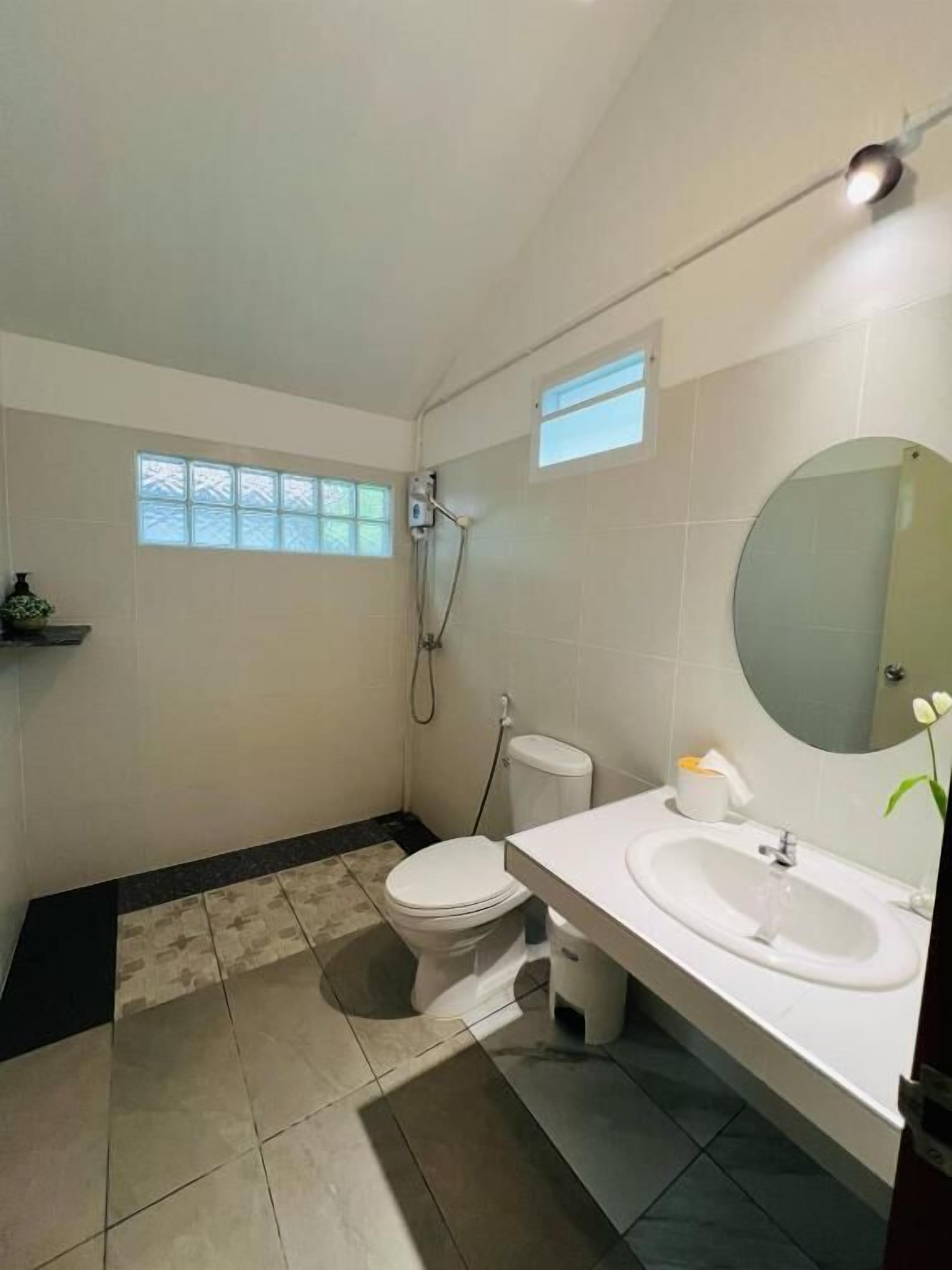A bathroom with a toilet, sink, and shower. There are two windows providing natural light.