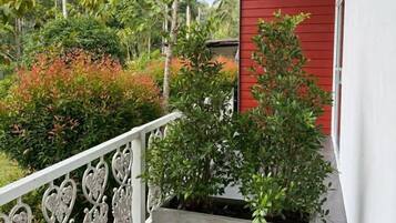 Un balcón con barandilla blanca, un edificio rojo y una jardinera con plantas verdes.