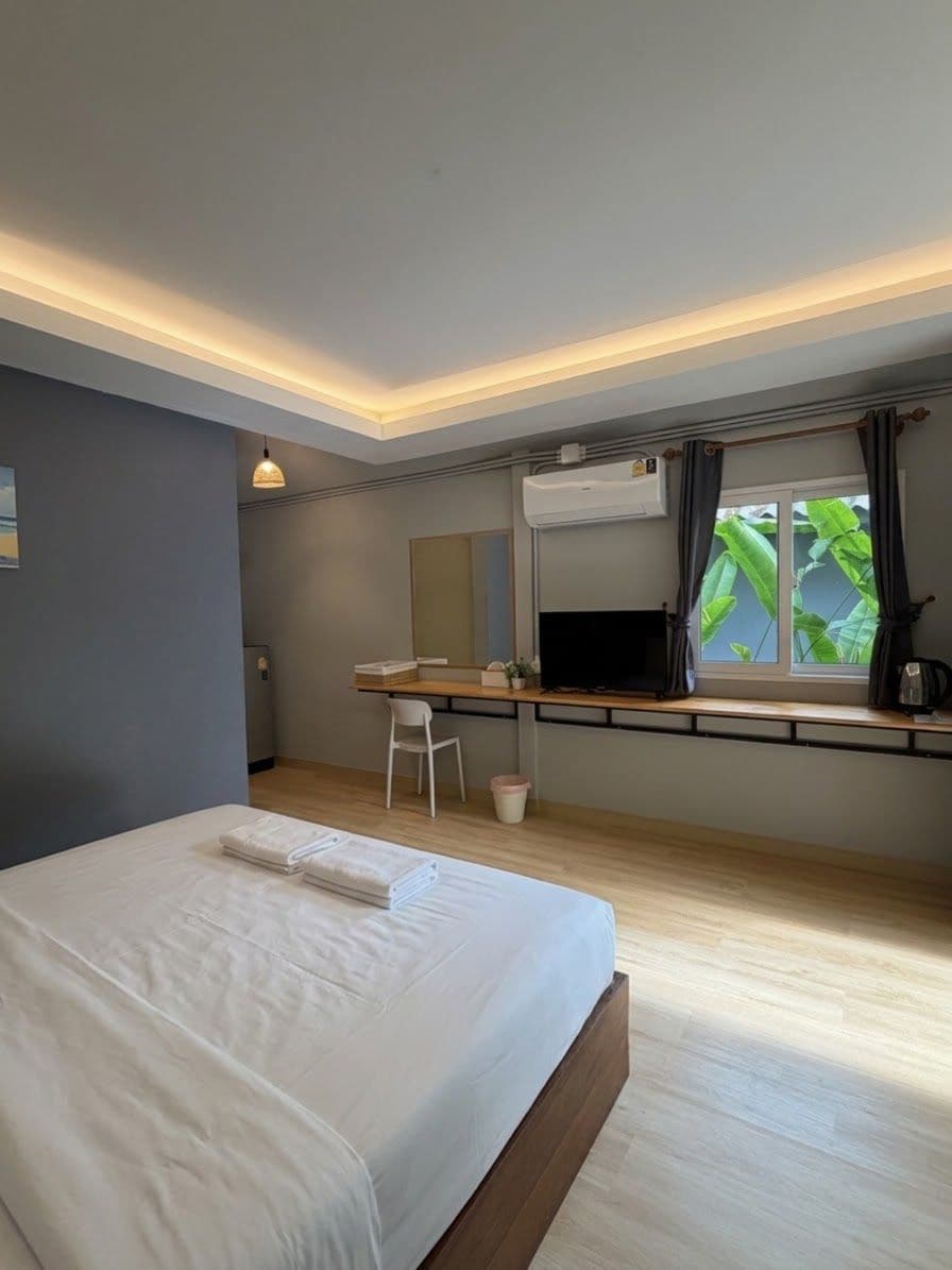A bedroom with a bed, a desk, a chair, a television, and a window with curtains.