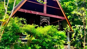 A triangular structure with a dark roof, surrounded by dense green foliage. - Zerohouse (Koh Kood)