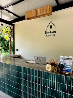 A reception desk with a 'Zero house HOME STAY' sign, a laptop, a QR code, and a welcome bag. - Zerohouse (Koh Kood)