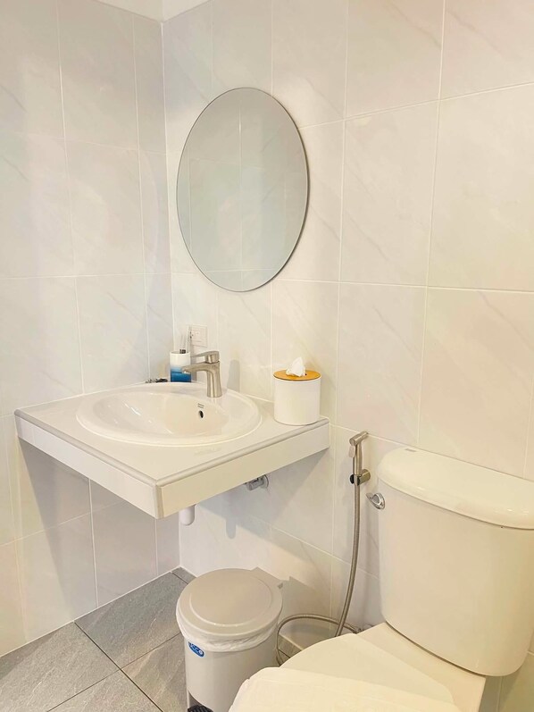 A bathroom with a white sink, mirror, toilet, and a trash bin.