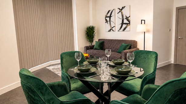 A dining area with a round glass table, green upholstered chairs, and a brown sofa in the background. - Modern 2 Bedroom Serviced Apartment West Street Sheffield (Sheffield)