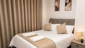A neatly made bed with a beige quilt, two pillows, and two folded towels. - Modern 2 Bedroom Serviced Apartment West Street Sheffield (Sheffield)