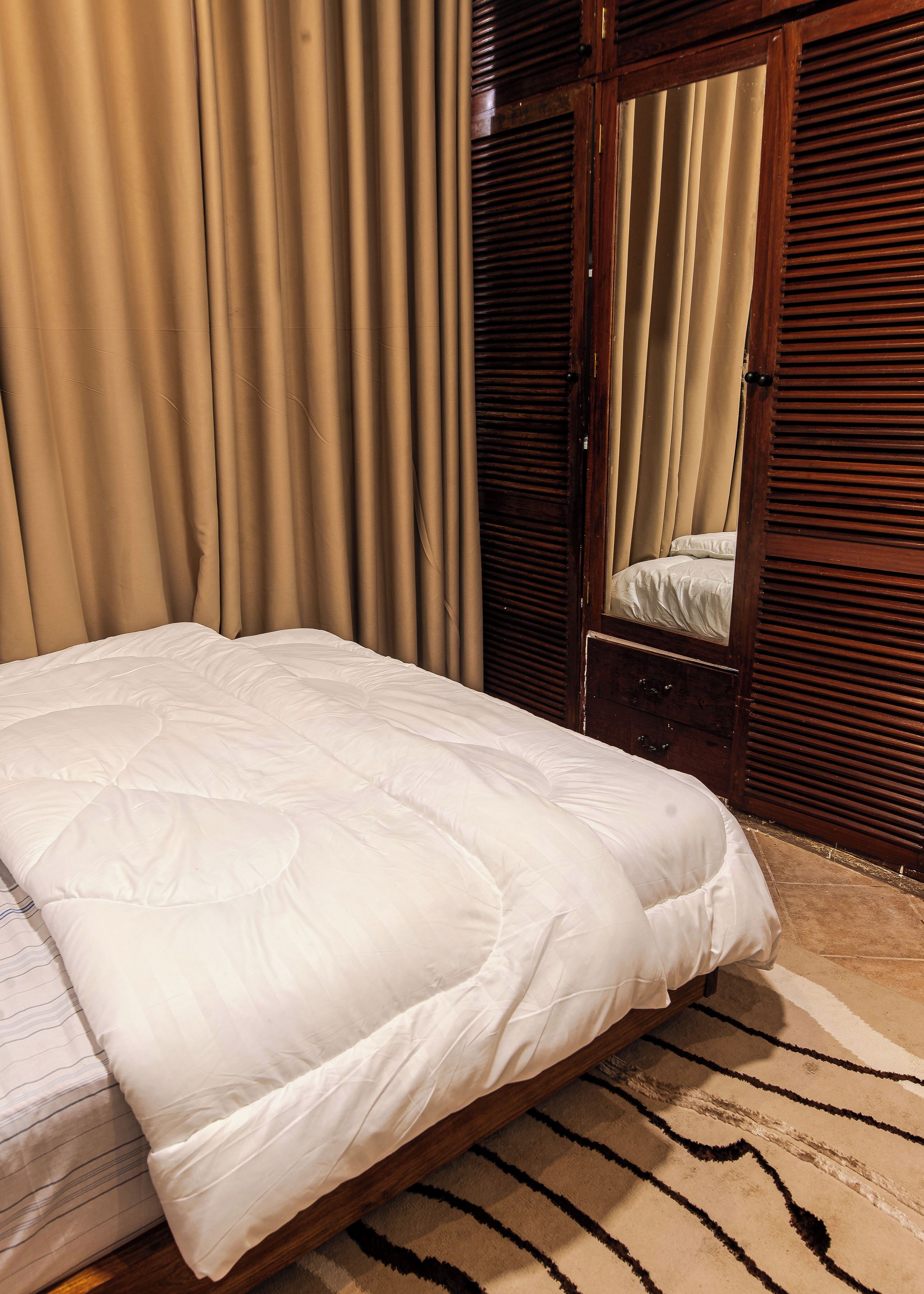 A bed with a white duvet, a wooden headboard, and a patterned rug.