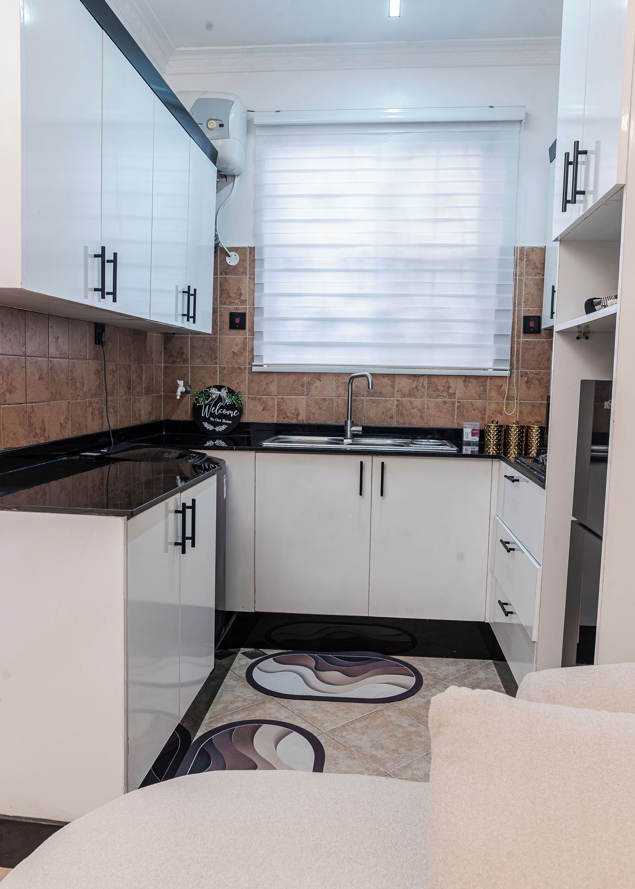 A compact kitchen with white cabinets, a black countertop, and a window with blinds.