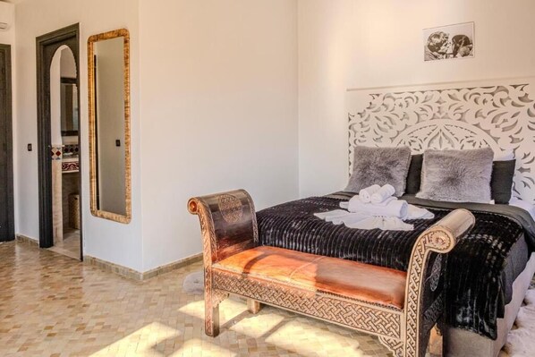 A bedroom with a large bed, a bench, a mirror, and a decorative headboard. - Luxury Villa with Pool & Gated Security (Marrakech)