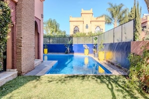 A swimming pool with a blue and white color scheme, surrounded by a well-maintained lawn and potted plants. - Luxury Villa with Pool & Gated Security (Marrakech)
