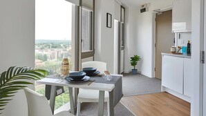 Una cocina moderna con armarios blancos, un comedor con mesa y sillas, y vista de la ciudad a través de amplios ventanales.