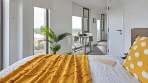 Habitación de hotel moderna con una cama grande, una zona de comedor y vistas a la ciudad.