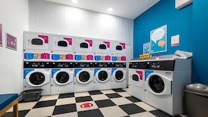 Un cuarto de lavandería con varias lavadoras y secadoras, suelo a cuadros y pared azul.
