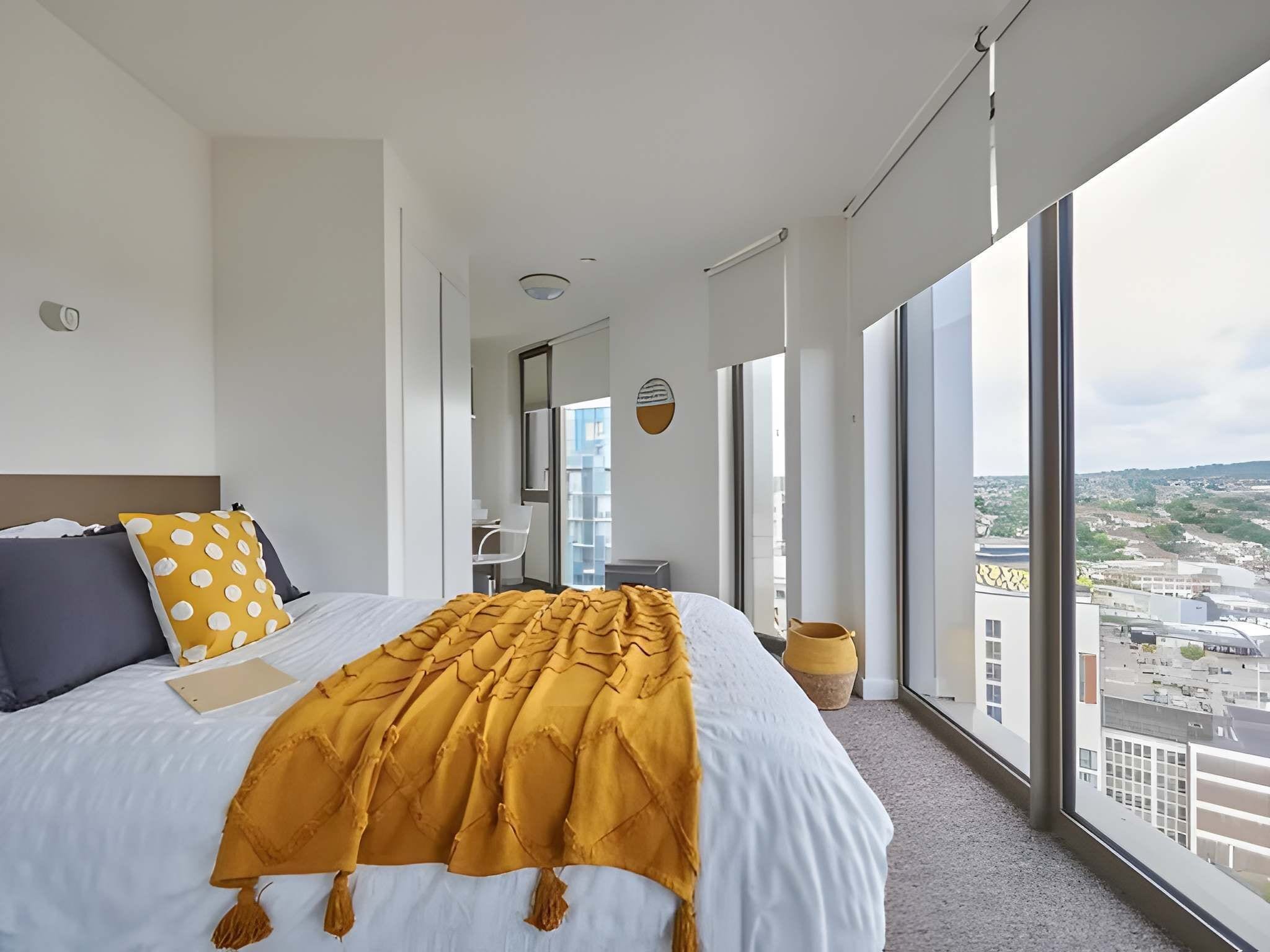 A hotel room with a large bed, a view of the city, and a window with a cityscape.