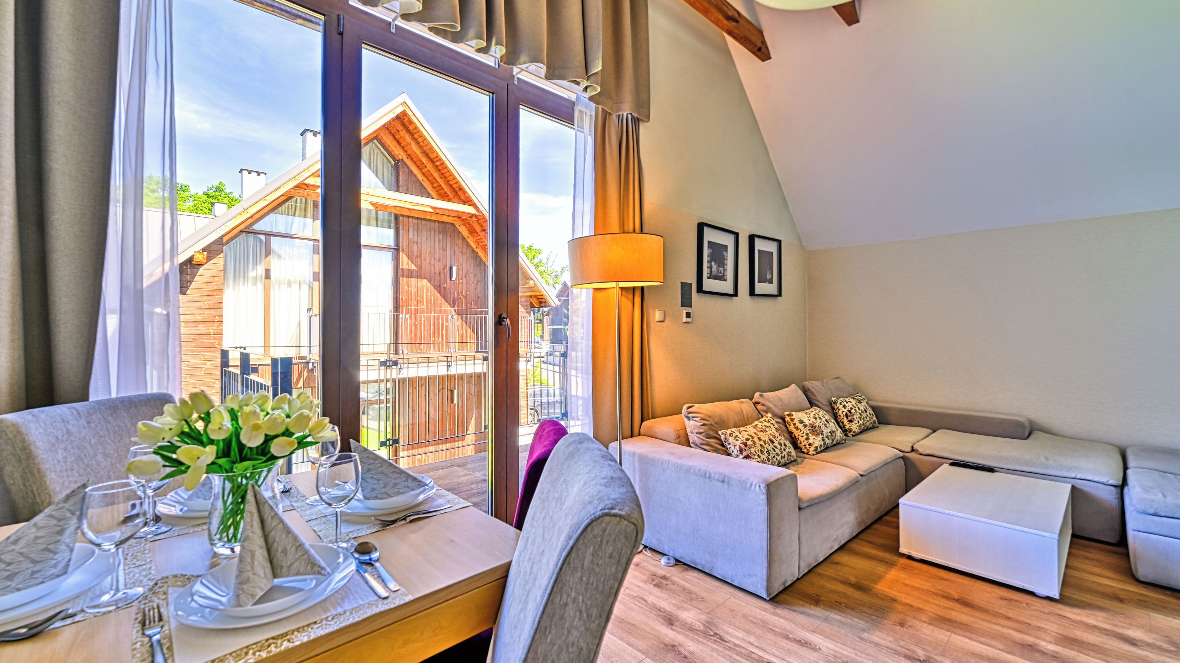 A modern living room with a dining area, large windows, and a view of a wooden building.