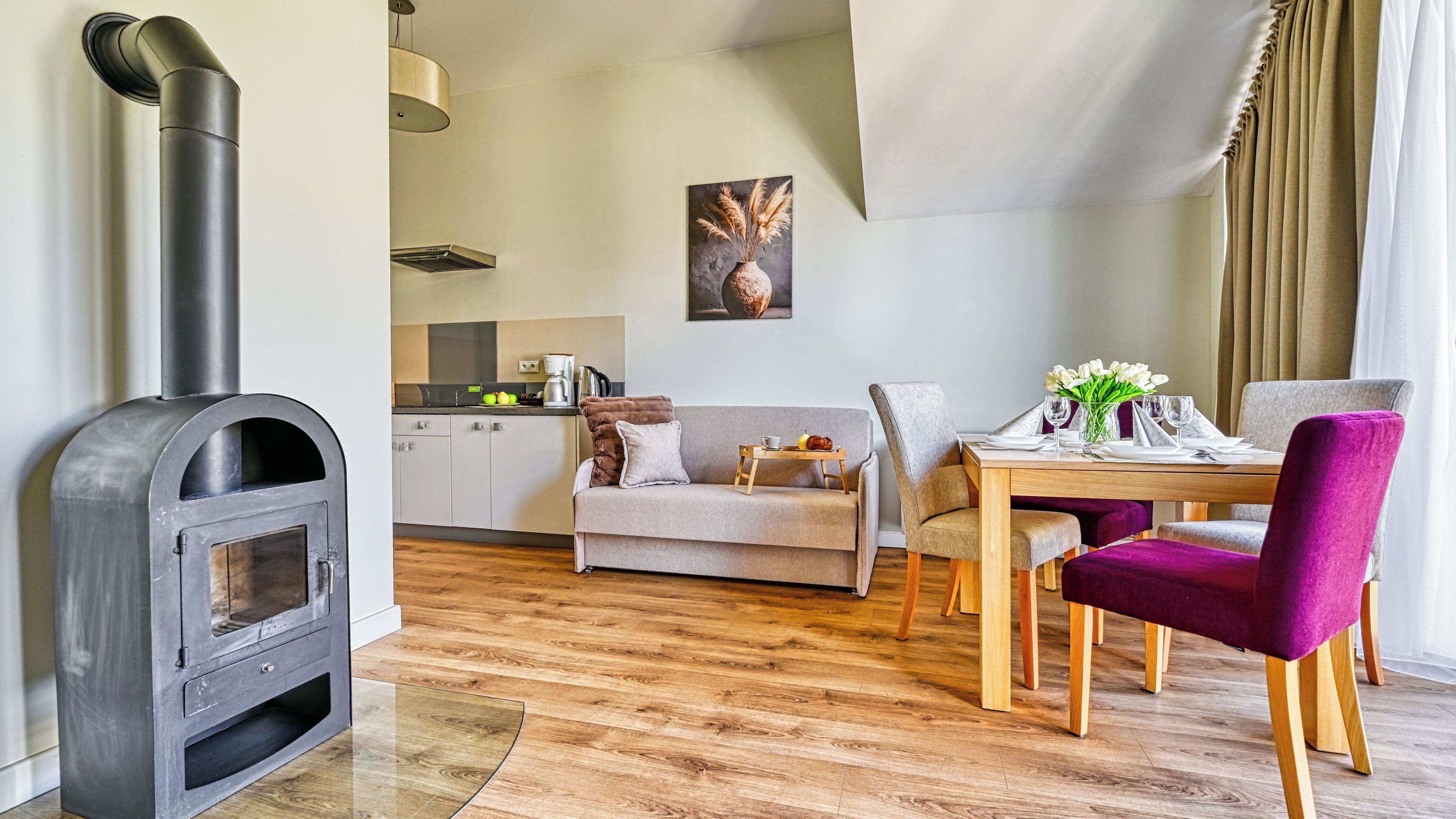 Ein modernes Wohnzimmer mit Kaminofen, Essbereich mit Tisch und Stühlen sowie eine Küche im Hintergrund.