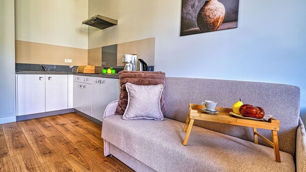 A modern living space with a sofa, a tray with a cup and fruit, and a kitchen in the background. - Apartamenty Sun & Snow Łomnica (Łomnica)