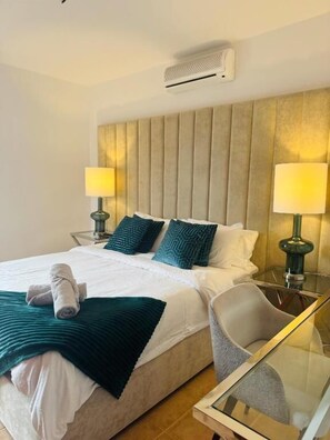 Ein Hotelzimmer mit einem großen Bett, zwei Nachttischlampen, einem Glastisch und einem modernen Kopfteil.