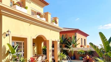 A two-story building with a swimming pool, outdoor seating, and various plants.
