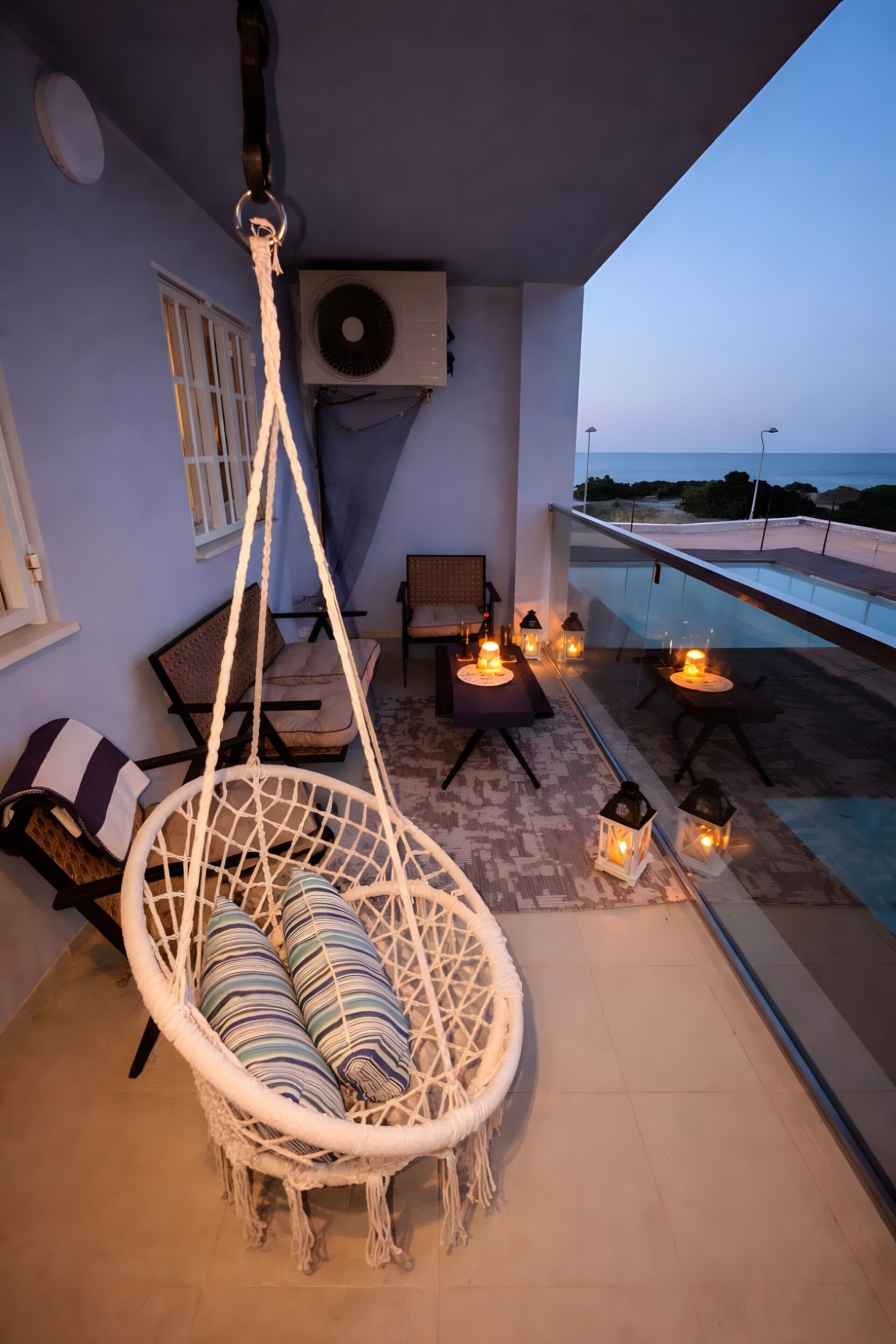 A balcony with a hanging chair, a pool, and outdoor lighting.