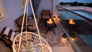 Un balcon avec un fauteuil suspendu, une piscine et un éclairage extérieur.