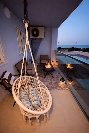 Un balcón con una silla colgante, una piscina e iluminación exterior.