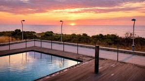 Une piscine avec une terrasse en bois et une vue sur le coucher de soleil sur l’océan.