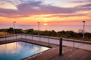 Una piscina con cubierta de madera y vista al atardecer sobre el océano.