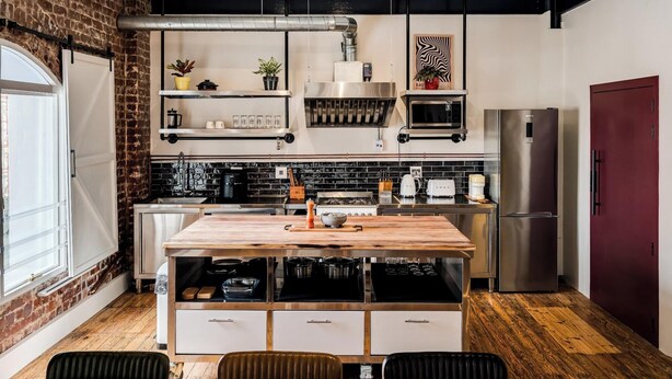 A modern kitchen with a wooden island, stainless steel appliances, and a brick wall. - Central City 2bed with Mountain Views Skywood Loft (Cape Town)