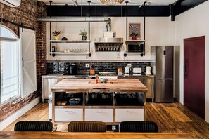 A modern kitchen with a wooden island, stainless steel appliances, and a brick wall. - Central City 2bed with Mountain Views Skywood Loft (Cape Town)