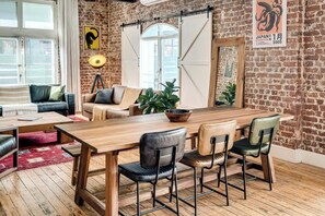 A room with a wooden dining table, four chairs, a sofa, and a large window. - Central City 2bed with Mountain Views Skywood Loft (Cape Town)