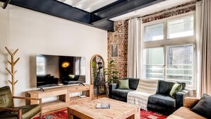 A modern living room with a television, a wooden coffee table, and seating. - Central City 2bed with Mountain Views Skywood Loft (Cape Town)