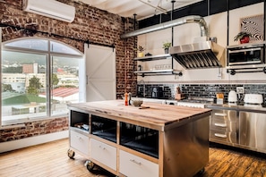 A modern kitchen with a brick wall, a large window, and a view of a cityscape. - Central City 2bed with Mountain Views Skywood Loft (Cape Town)