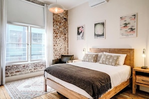 Ein Schlafzimmer mit Backsteinwand, einem großen Bett mit Holz-Kopfteil, einem Nachttisch und einer Pendelleuchte.